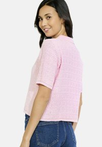 Gaiši rozā īsais džemperis ar īsām piedurknēm, ribots tekstūras raksts un vaļīgs aušanas paraugs. Kombinēts ar zilu džinsa biksēm.