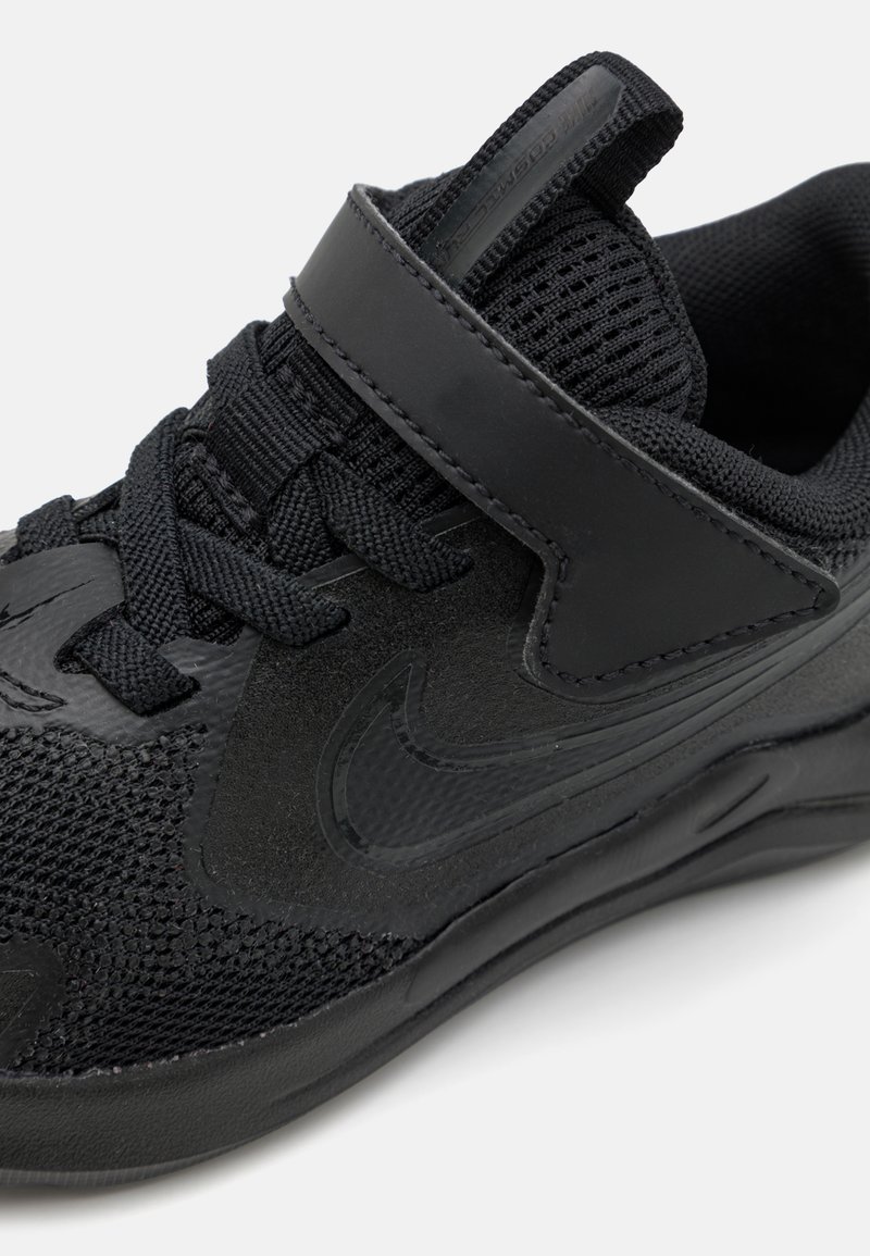 Zapatilla deportiva negra con materiales de malla y sintéticos, que incluye cordones, una correa de velcro y una suela texturizada. Acabado suave y duradero.