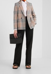 Dubbelzijdige geruite blazer in grijs en oranje, gecombineerd met een witte blouse, zwarte broek en een zwarte clutch. Draag het met platte sandalen.