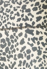Tissu à motif léopard en gris et crème avec une texture lisse. Présente une couture visible cousue dans une teinte contrastante.