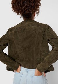 Mörkgrön mockajacka med en figursytt design, kort längd och dragkedjeaccent på ärmarna, med en slät och mjuk textur.