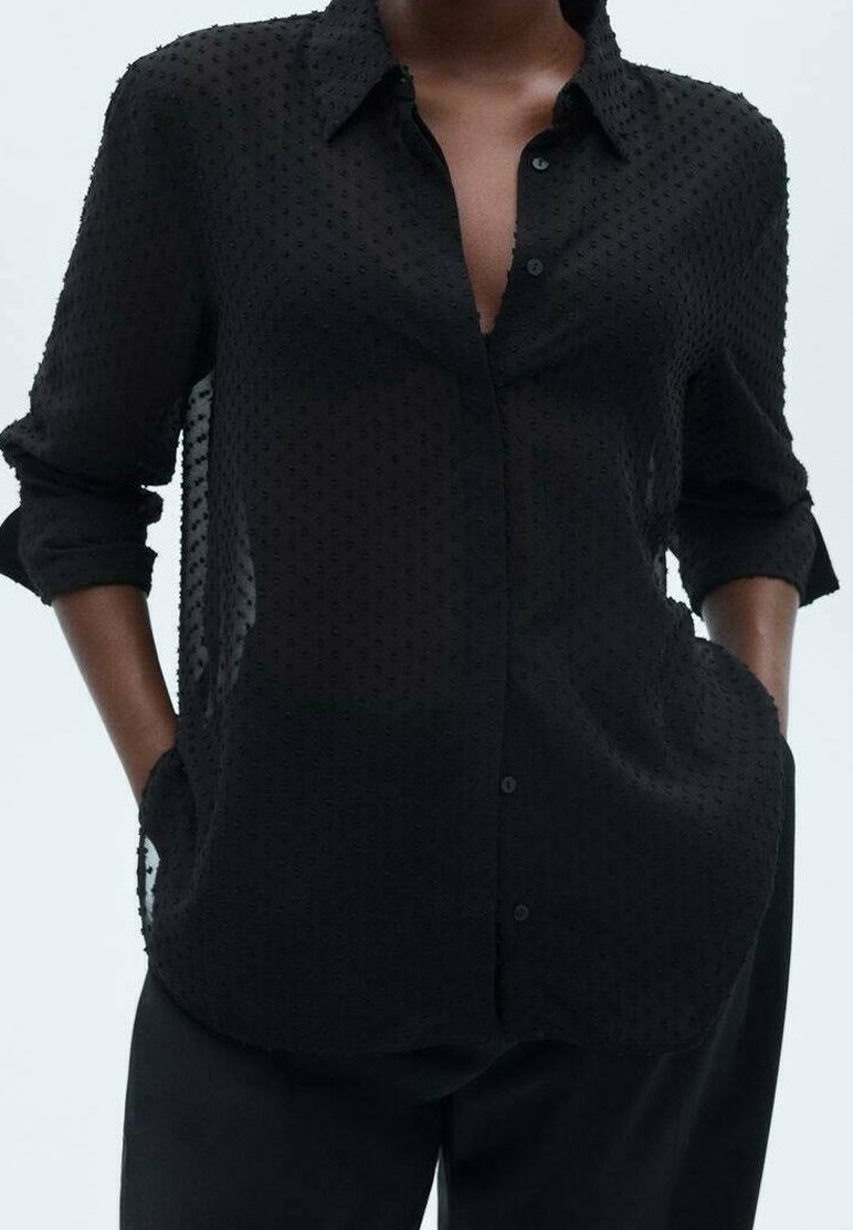 Camicia nera trasparente con pattern testurizzato, maniche lunghe, colletto e tasche ai lati. Progettata per una vestibilità ampia.