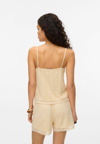 Beige hæklede top med tynde stropper, prydet med et cirkulært mønster og bølgede kanter, parret med matchende shorts.