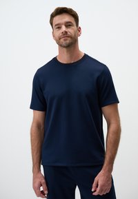 Granatowa koszulka z krótkim r ękawem z miękkiego materiału, z okrągłym dekoltem i detalami w postaci szwów, połączona ze spodniami w dopasowanym kolorze.