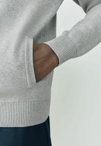 Hellgrauer Strickpullover mit gerippten Bündchen und Saum, ausgestattet mit einer seitlichen Tasche, die eine glatte Textur und eine enganliegende Passform zeigt.