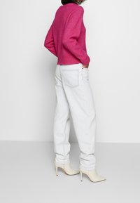 Suéter de punto fucsia con puños acanalados, combinado con jeans baggy azul claro. La modelo lleva botas de tacón puntiagudas en color crema.