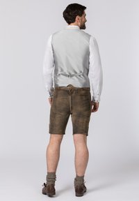 Graue ärmellose Weste über einem weißen Langarmshirt, kombiniert mit braunen Shorts und gestrickten knielangen Socken, von hinten betrachtet.