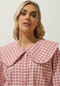 Rosa gingham-skjorta med en stor volangkrage, med knappar framtill. Tyget har en mjuk textur och en lätt lyster.