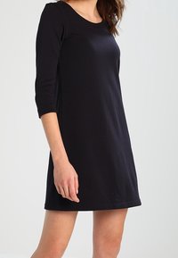Vestido negro ajustado con mangas de tres cuartos, escote redondo y una textura suave. Longitud a la rodilla sin patrones ni adornos visibles.