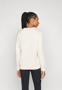 Felpa chiara con una vestibilità rilassata, spalle scese e polsini a costine; indossata con leggings neri, vista da dietro.