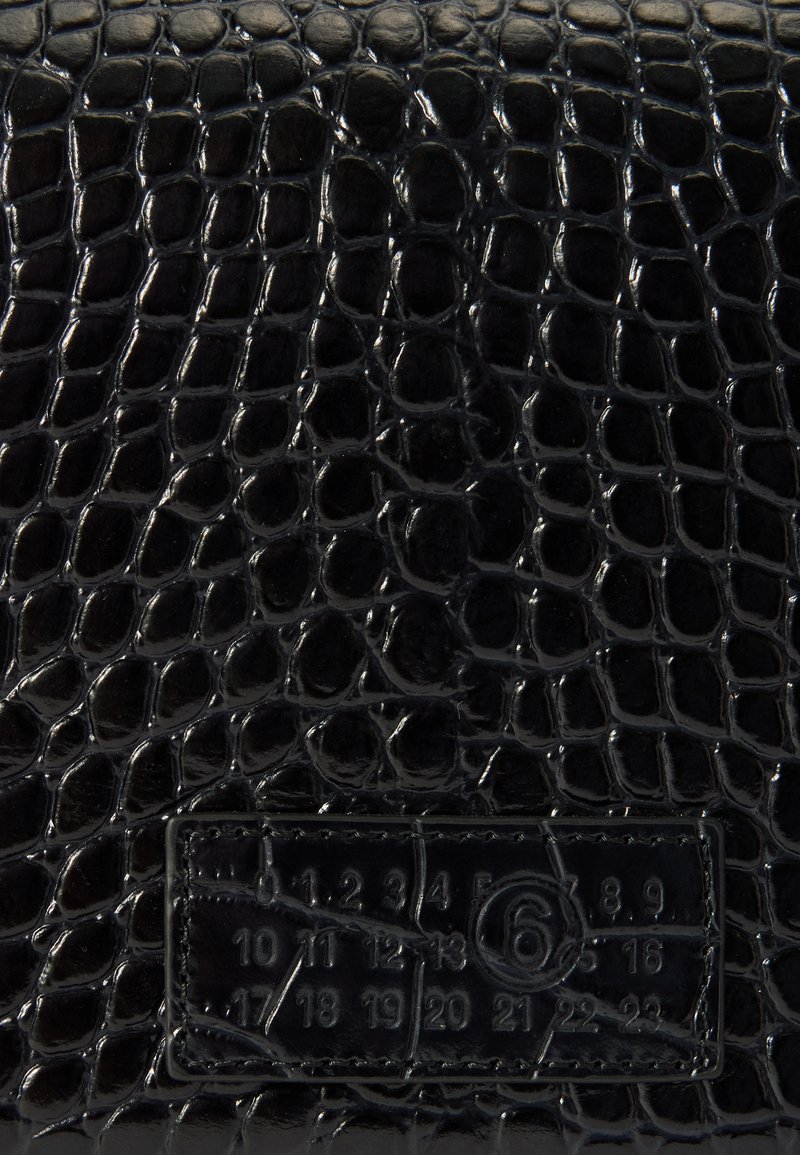 Pelle nera testurizzata con finitura lucida, caratterizzata da un motivo in pelle di coccodrillo e un'etichetta rettangolare con numeri e un logo circolare.