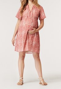 Gravidklänning i rött och vitt texturerat mönster, med korta ärmar, V-ringning och resår i midjan för komfort.