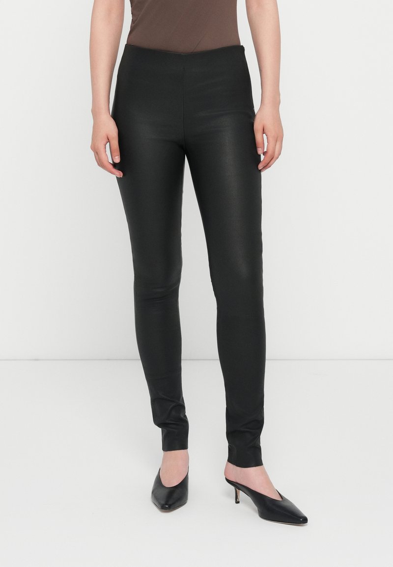 Leggings noirs en simili cuir avec une taille haute, un design ajusté, une texture lisse et une coupe aux chevilles, accompagnés de mules noires.