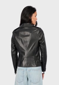 Černá kožená bunda se strukturovaným střihem, ostrým límcem a zipovými manžetami. Hladká textura s viditelnými švy, stylizováno pro přiléhavý vzhled.