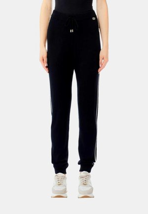 Pantaloni da jogging neri con cintura a coste, chiusura con cordoncino e strisce laterali bianche. Il materiale sembra morbido e ha una vestibilità rilassata.