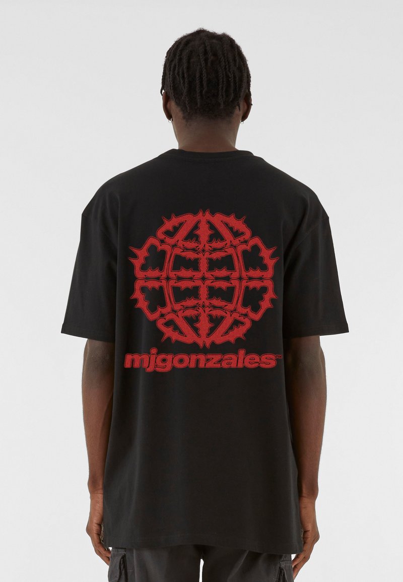 Schwarzes oversized T-Shirt mit einem großen roten Grafikdesign auf der Rückseite, das Text und abstrakte Formen enthält, aus Baumwollmaterial gefertigt.