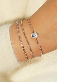 Trio di bracciali in argento composto da una catena liscia, una catena con maglie testurizzate e una con un pendente ottagonale caratterizzato da un design a stella.