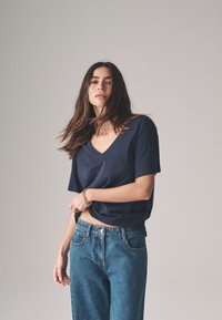 Marineblauw T-shirt met V-hals van zachte stof, korte mouwen, losse pasvorm, gecombineerd met high-waisted blauwe jeans met voorzakken en een klassieke knoopsluiting.