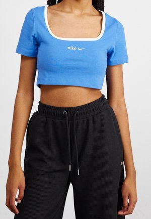 Blå croppet t-shirt med firkantet halsudskæring og hvid kant, med en lille hvid Nike-logo på brystet. Sorte ribstrikkede joggers med snøre i taljen.
