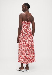 Rotes Maxikleid mit weißen Blumenmustern, Spaghettiträgern und einem Rückengeknüpfte Detail. Glatter Stoff mit fließender Silhouette.