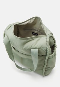 Plyšová zelená látková taška se dvěma uchy, zipovým vrškem a vnitřní kapsou. Hladký povrch a zaoblený tvar s přitahovanými akcenty.