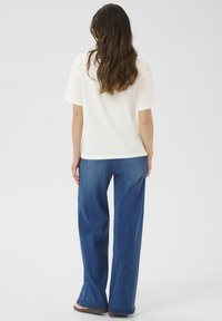 Hvid kortærmet top parret med h�øjtaljede, brede blå jeans. Jeansene har en falmet tekstur med en let flare ved sømmen.