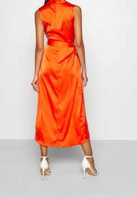 Pomarańczowa sukienka bez rękawów z satyny, z dopasowanym gorsetem, talią podkreśloną paskiem i rozkloszowanym dołem sięgającym poniżej kolan. Noszona z białymi sandałami na obcasie.