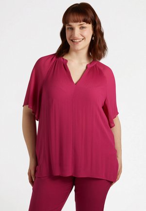 Top magenta con design plissettato, scollatura a V e maniche corte, realizzato in un tessuto liscio. Indossato con pantaloni magenta coordinati.