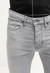 Jeans de denimo gris con un diseño ajustado. Incluyen cinco bolsillos, una cremallera frontal y detalles de costura sutiles.