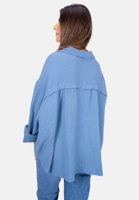 Hellblaues Hemd mit Knopfleiste aus strukturierter Baumwolle, das eine lockere Passform, lange Ärmel und ein Rückenteil mit Passe aufweist. Lässiges und oversized Design.