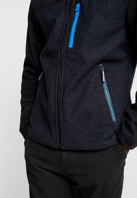 Chaqueta negra con cremallera y acentos azules, fabricada en un tejido texturizado. Presenta dos bolsillos con cremallera y un cuello alzado.