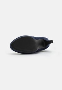 Stivaletto alla caviglia in suede blu navy con suola in gomma nera liscia, caratterizzato da un motivo scanalato per una migliore trazione e un inserto per facilitare la calzata.