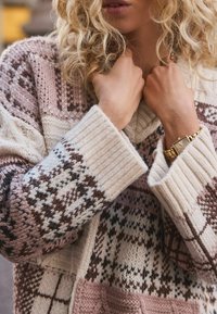 Knit sweater featuring a mix of cream, pink, and brown hues with geometric patterns, ribbed cuffs, and a relaxed neckline.