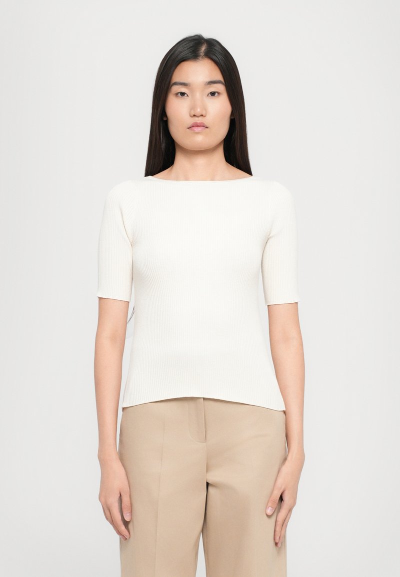 Top bianco a costine con maniche corte, scollatura rotonda e silhouette aderente, abbinato a pantaloni beige a gamba larga.