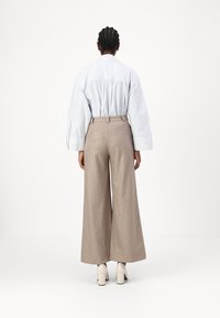 Light blue striped cotton shirt with oversized sleeves, paired with beige wide-leg trousers. The trousers have a textured finish and back pockets.