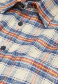 Zachte flanellen shirt met een rood, blauw, geel en crème ruitpatroon, zwarte knopen en een zichtbare borstzak en kraag.