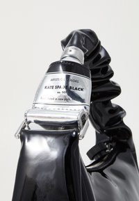 Mustan läikivad kott, millel on kortsus käepide, hõbedane riistvara ja sildil on tekst "KATE SPADE BLACK". Ühtlane tekstuur kogu ulatuses.