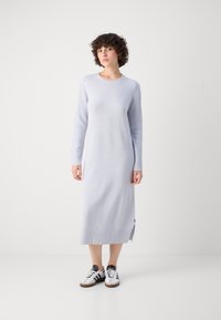 Lyseblå langermet strikket kjole med ribbede ermer og hem, med en sideslitasje. Kombinert med svart-hvite joggesko.