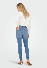 Tievās zilo džinsu bikses ar augstu jostasvietu, ar divām aizmugurējām kabatām un brūnu ādas birku. Saskaņotas ar baltu blūzi un brūnām papēžkurpēm.