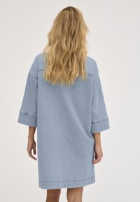 Robe en denim bleu clair au style décontracté, avec des manches trois-quarts et une silhouette droite. Présente des coutures contrastantes et des poches latérales.