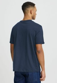 Tamsiai mėlyna medvilnės marškinėliai trumpomis rankovėmis, apvaliu kaklu, laisvo kirpimo, su lygiu paviršiumi ir be matomų raštų ar grafikos.