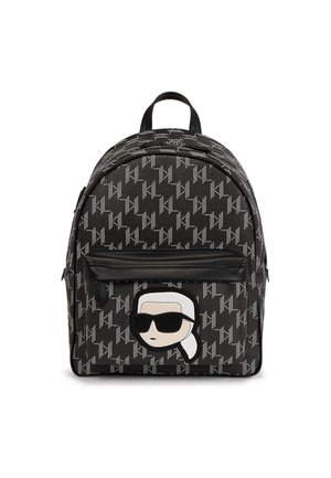 Mochila negra con patrón repetitivo blanco KL y bolsillo frontal que presenta una cara de dibujo animado con cabello blanco y grandes gafas de sol negras.