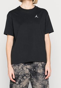 Sort bomulds T-shirt med rund hals, korte ærmer og et lille hvidt Jumpman-logo over venstre bryst, båret med mønstrede cargo-bukser.