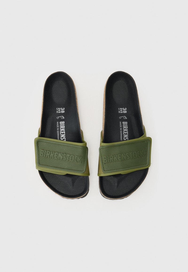 Des sandales glissantes vertes avec un dessus en caoutchouc présentant des accents texturés et un marquage en relief, posées sur une semelle noire avec des détails en liège.
