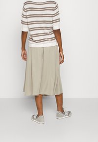 Gestreifter beiger und weißer Strickoberteil mit kurzen Ärmeln, kombiniert mit einem hellbeigen, gefältelten Rock und grauen New Balance Turnschuhen.
