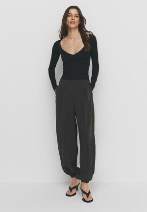 Must pikkade varrukatega pluus V-kaelusega, kombineeritud tumedate lahtiste pükstega, millel on voldid ja küljetaskud. Kanditud mustade varbavaheplätudega.