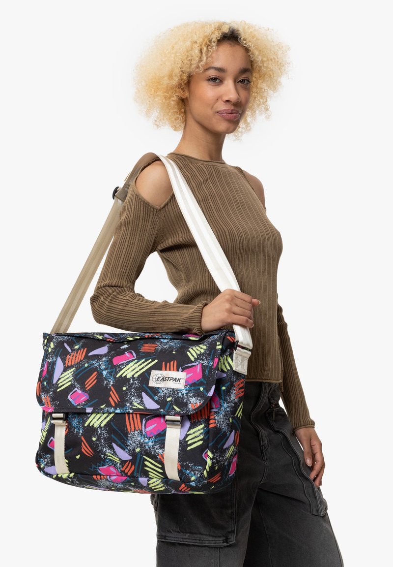 Sac messager Eastpak avec un tissu noir orné de motifs abstraits colorés. Il dispose d'une fermeture à rabat et d'une bandoulière réglable.