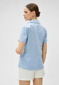 Camisa de manga corta azul claro con cuello clásico. Tejido suave y ligero, con un corte entallado. La parte trasera tiene un dobladillo curvado.