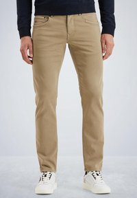 Pantalones chinos beige de corte ajustado, con bolsillos delanteros, cintura con trabillas para cinturón y costuras en contraste, combinados con zapatillas blancas.