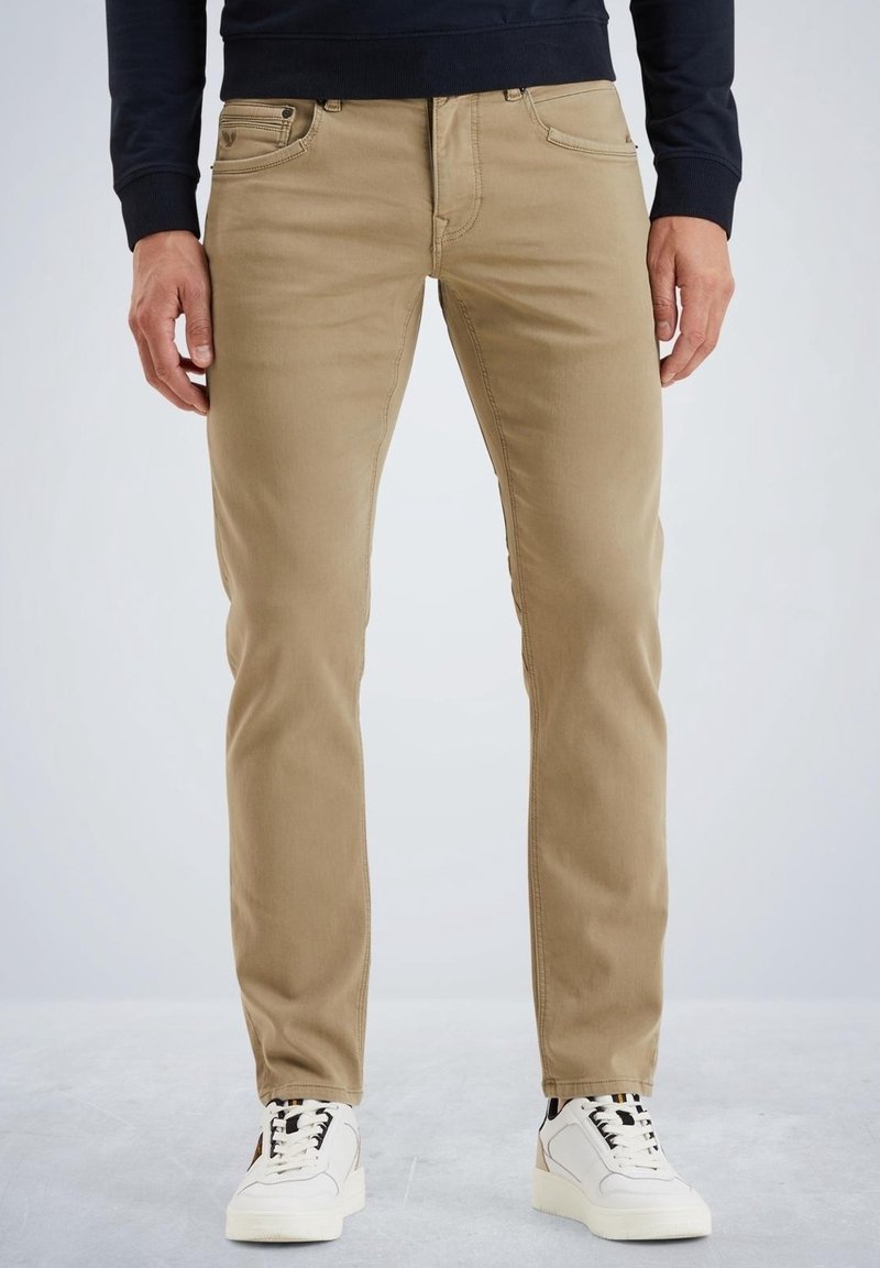 Pantalones chinos beige de corte ajustado, con bolsillos delanteros, cintura con trabillas para cinturón y costuras en contraste, combinados con zapatillas blancas.